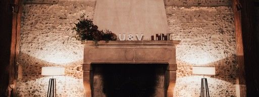 A fire burns in a beautiful old fireplace decorated with the initials "U and V" on the mantle above.