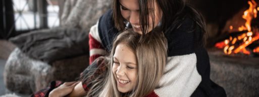 Mother hugs her daughter as they lie near the fireplace